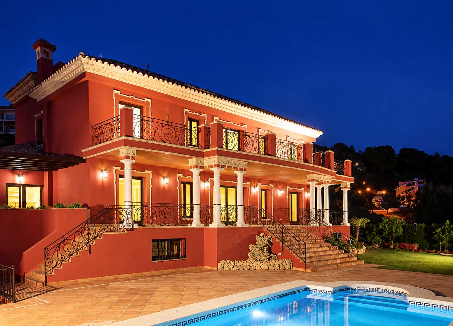 Villa de fachada roja iluminada de noche con terraza y piscina en la Costa del Sol