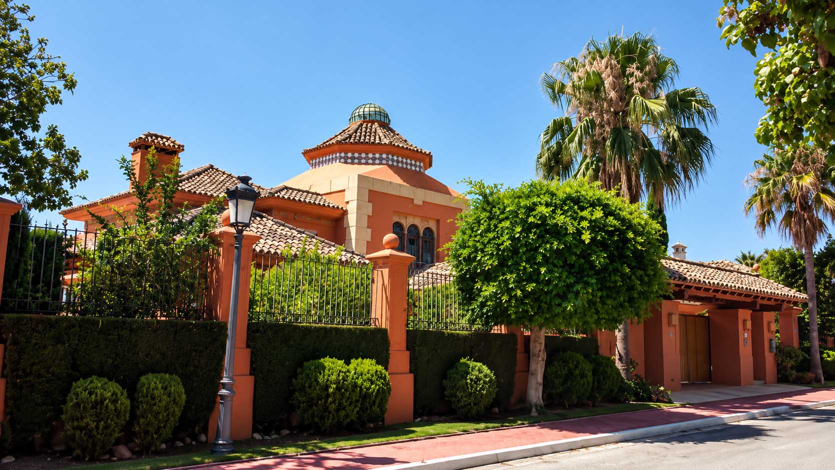 Vivienda de fachada naranja con jardín, setos y palmeras en la Costa del Sol