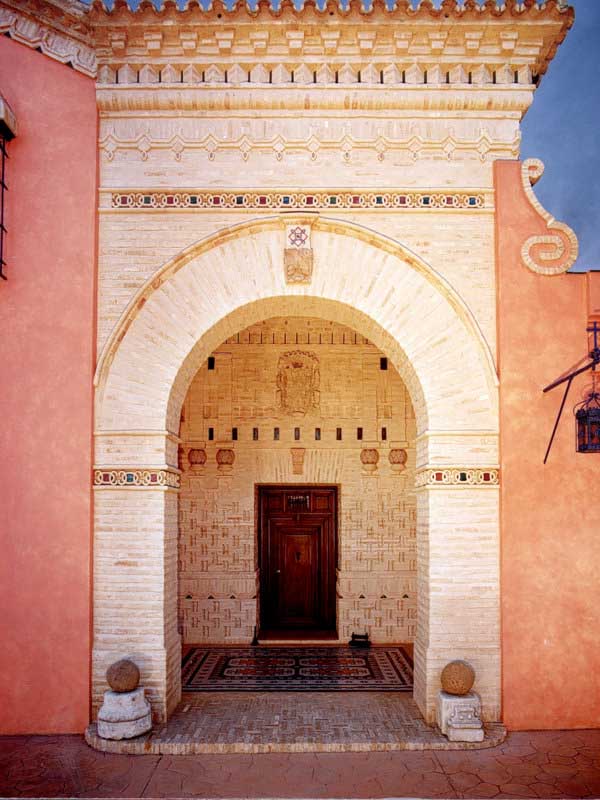 Entrada con arco de ladrillo y puerta de madera en una fachada de color teja