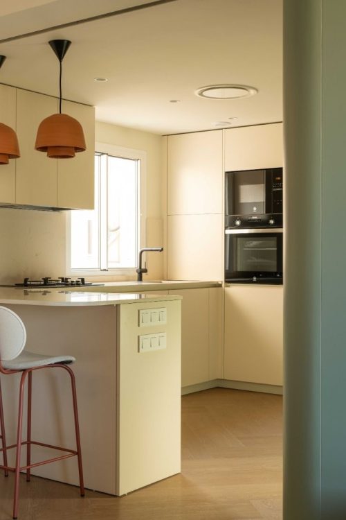 Cocina abierta con península, taburetes y lámparas colgantes naranjas tras la reforma de la vivienda