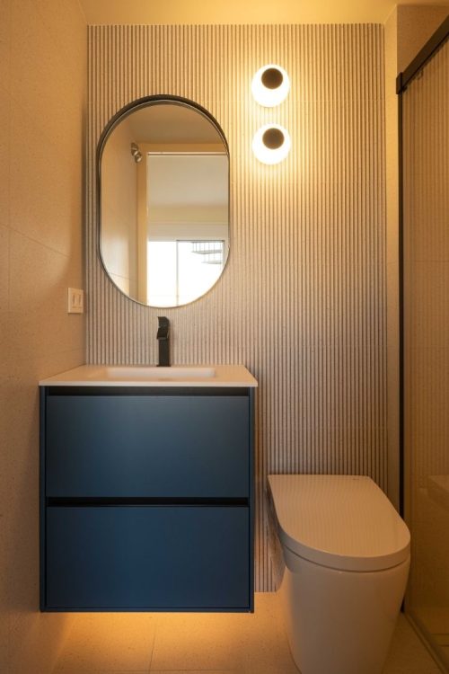 Baño con mueble suspendido azul, espejo ovalado y apliques de luz