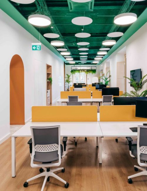 Zona de trabajo con mesas compartidas, techo verde con focos y arco naranja en Uptodown